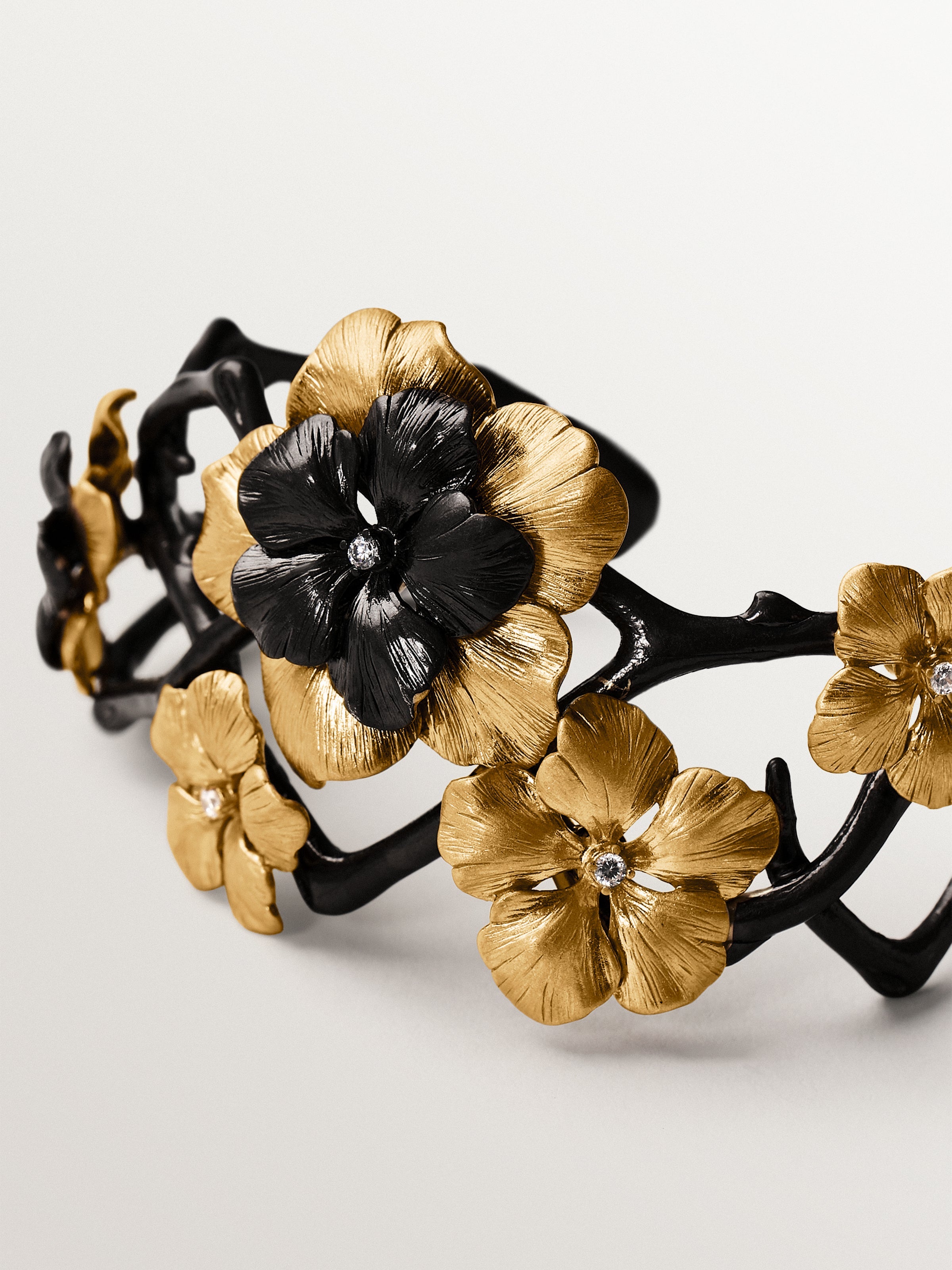 Pulsera rígida bicolor bañada en oro amarillo con cristales y motivo de flor