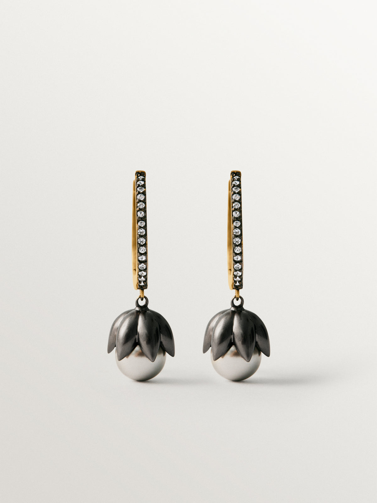 Pendientes bicolor de aro bañados en oro amarillo con acabado gunmetal, cristales blancos y grises en forma de flor