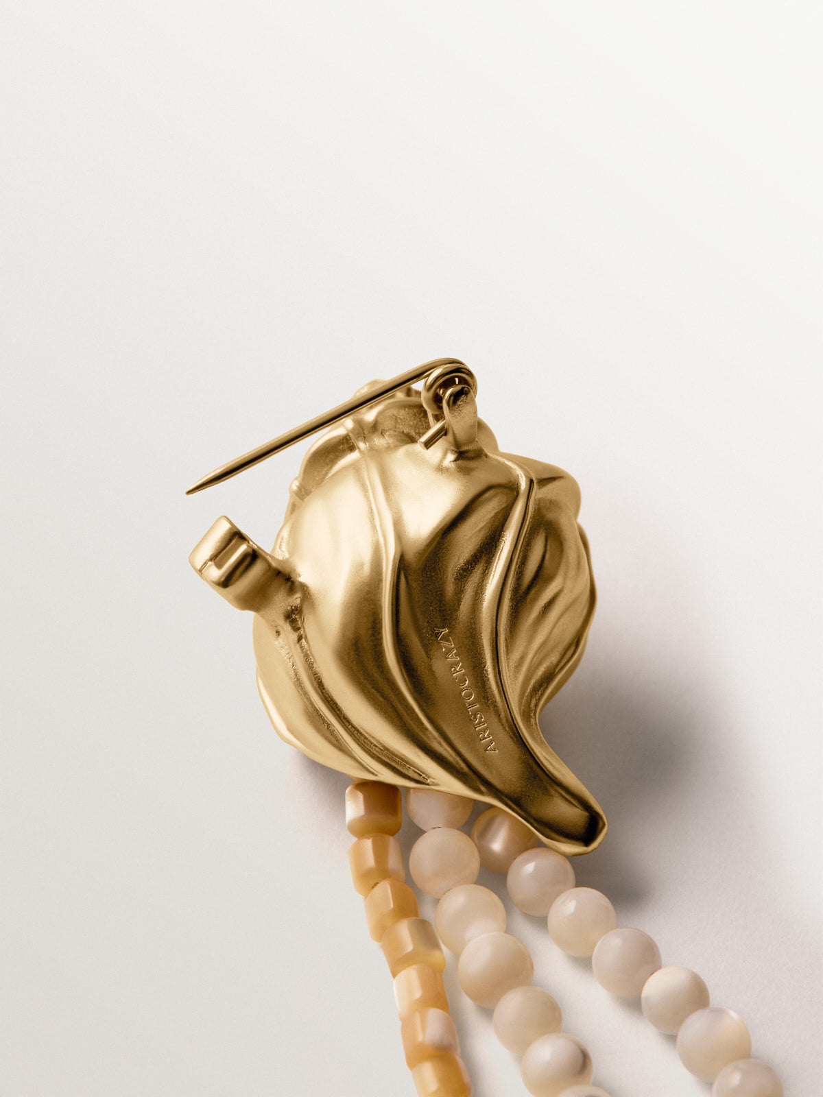 Broche bañado en oro amarillo con cristales, bolitas blancas y forma de concha