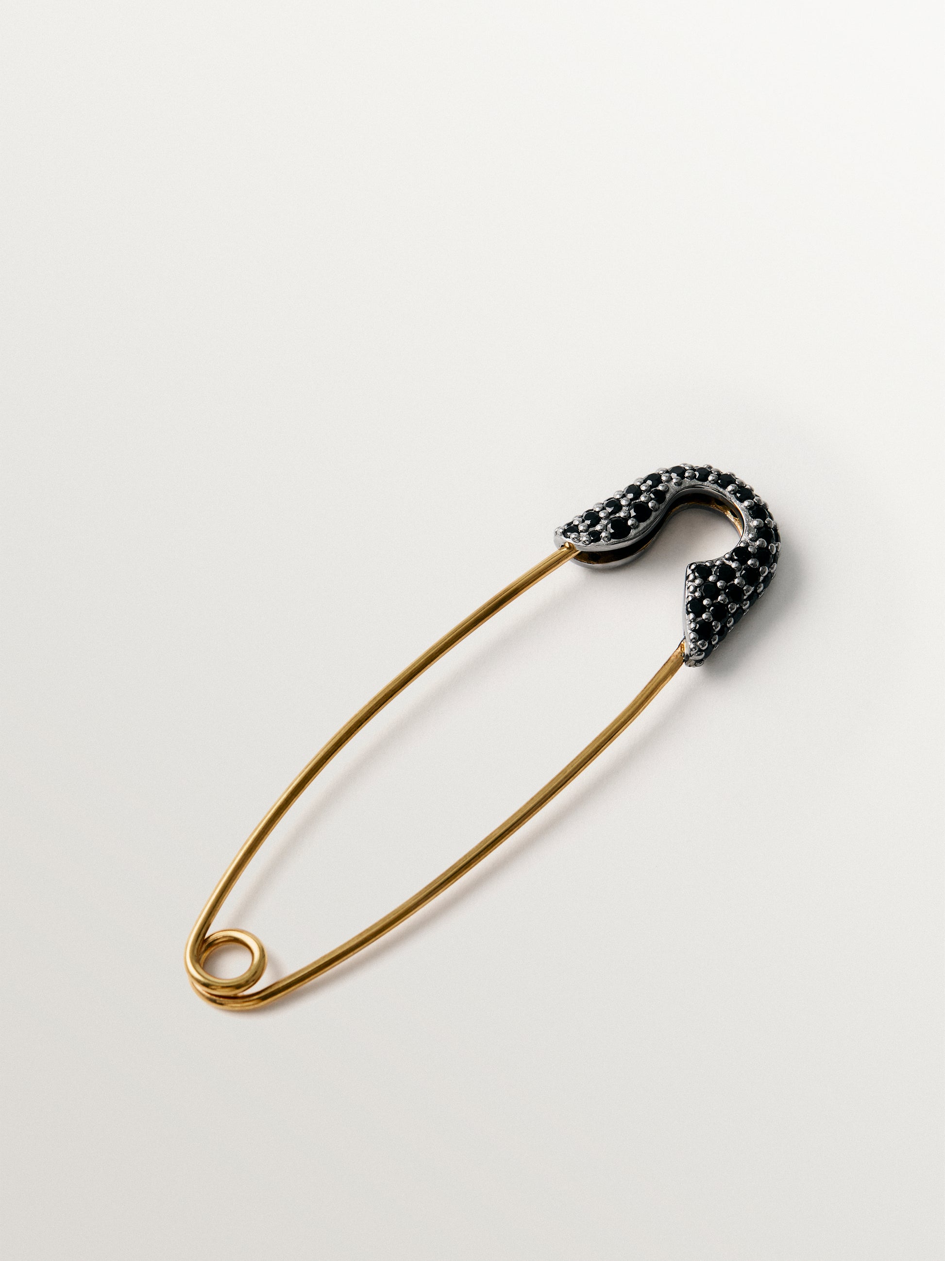Charm bañado en oro amarillo con espinelas negras y forma de imperdible