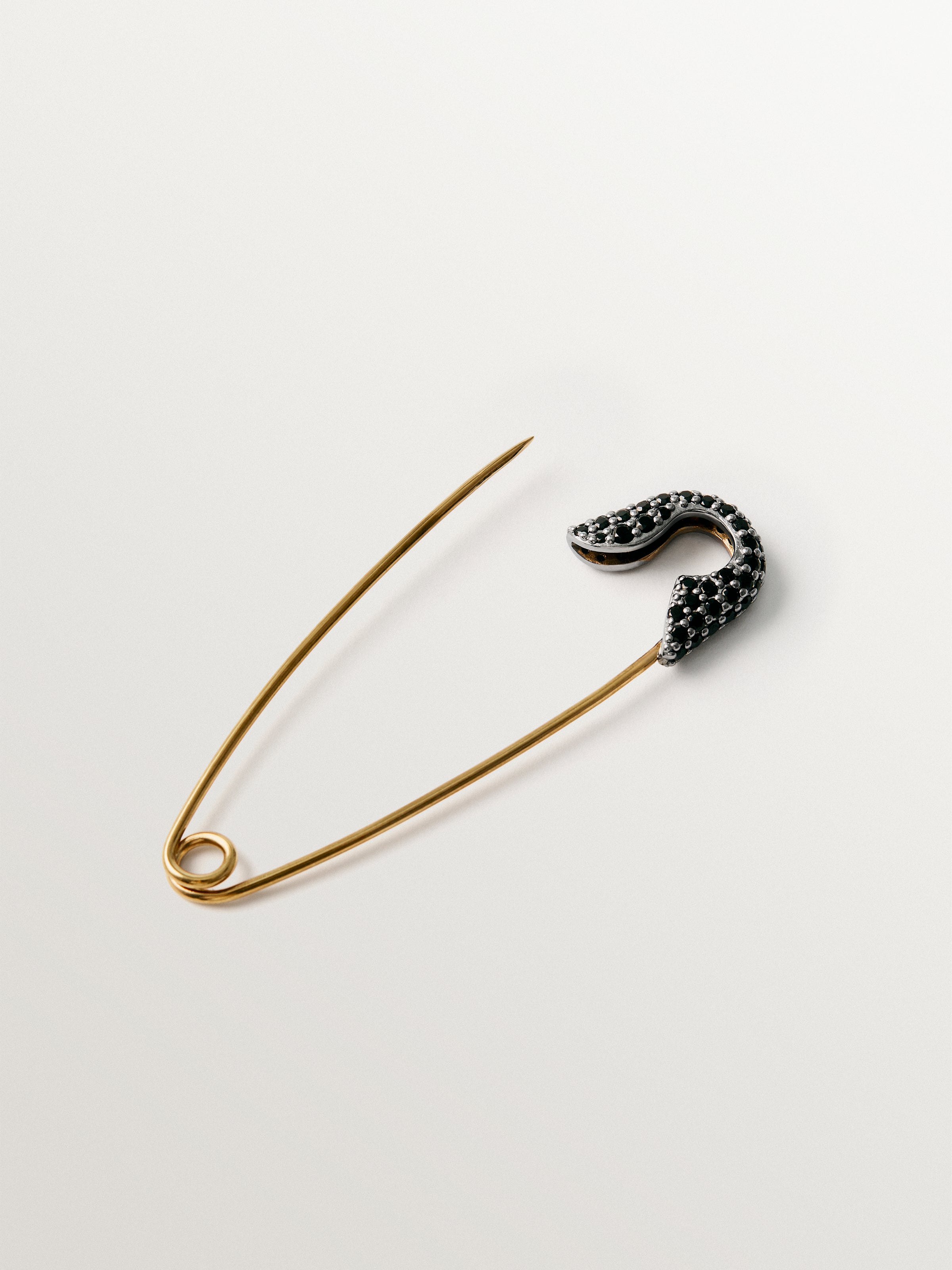 Charm bañado en oro amarillo con espinelas negras y forma de imperdible