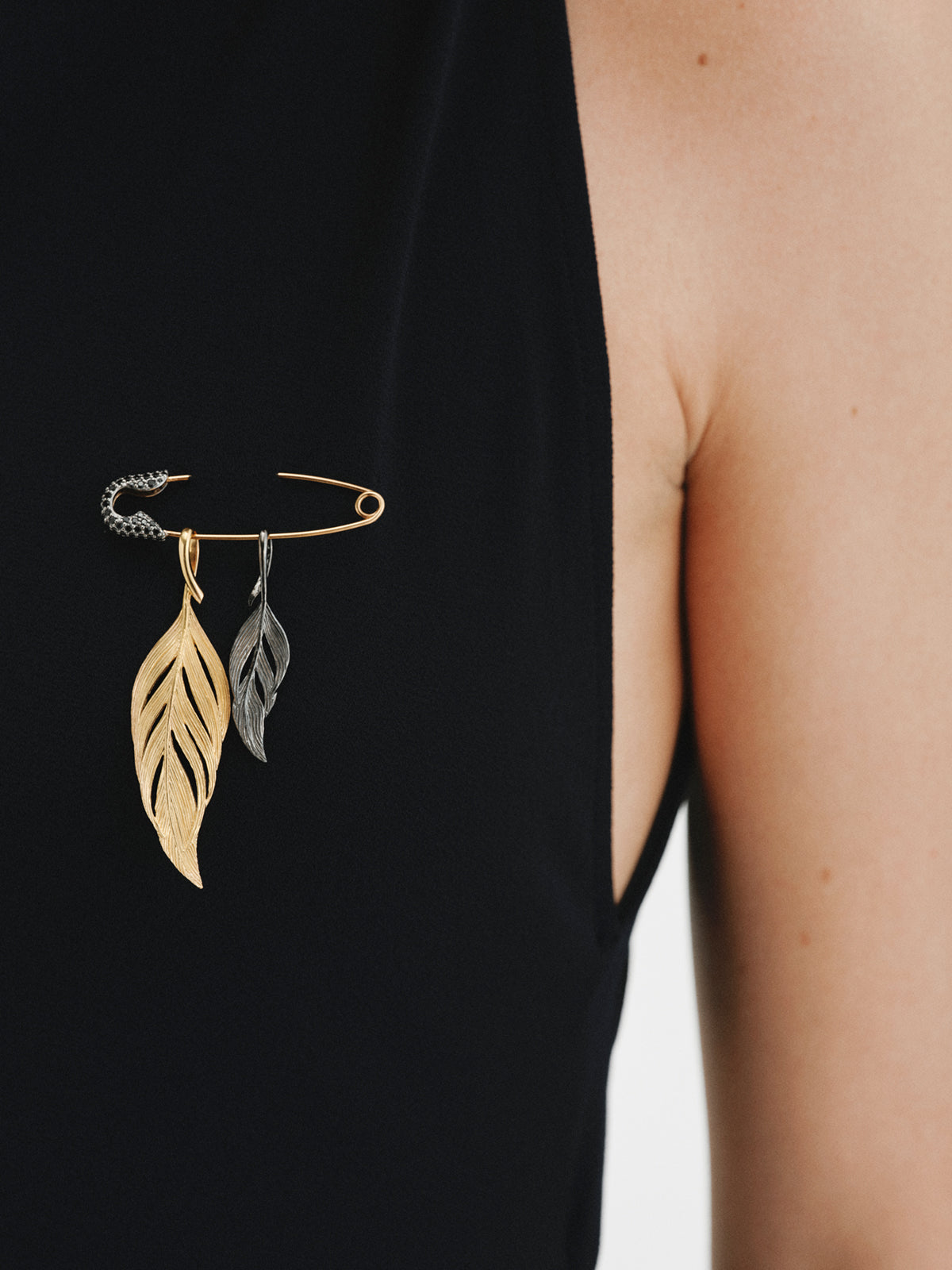 Charm bañado en oro amarillo con espinelas negras y forma de imperdible