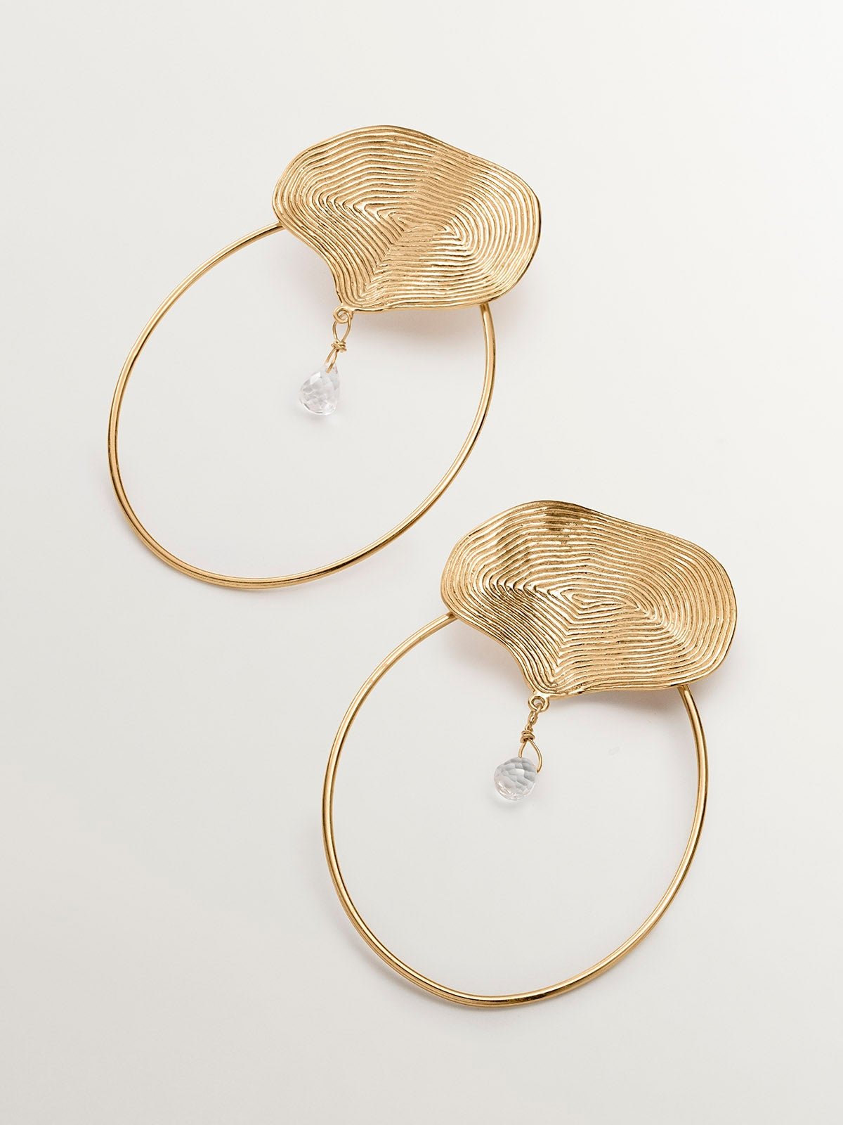 Boucles d'oreilles créoles en argent 925 plaqué or jaune 18K avec relief et topaze blanche.