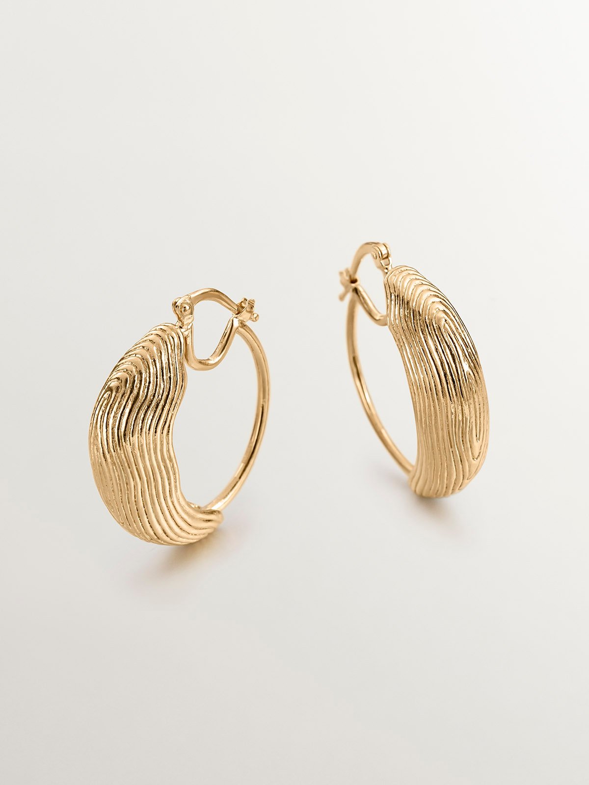 Medium hoop earrings made of 925 silver coated in 18K yellow gold with relief and irregular shape.