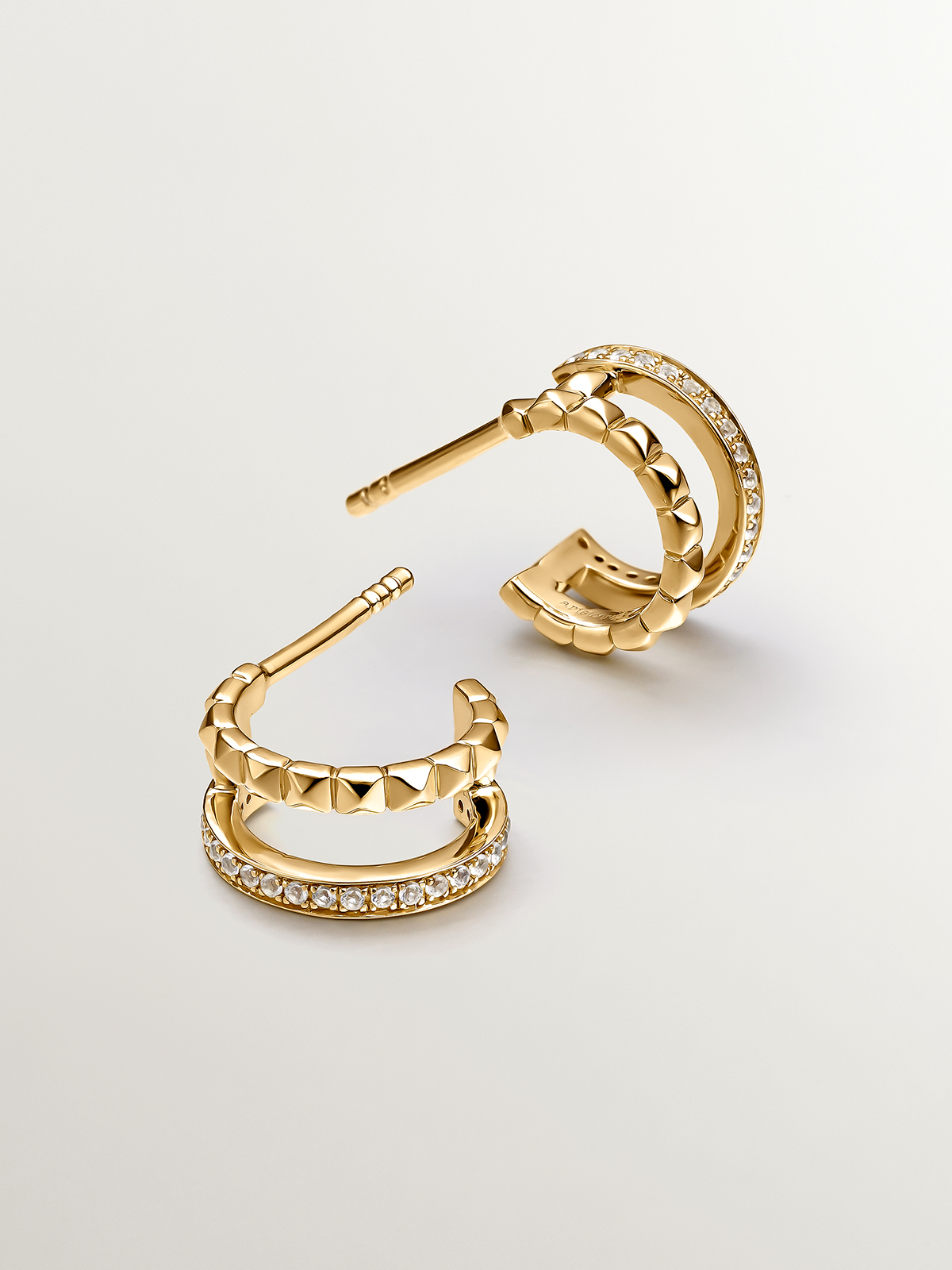 Small double hoop earrings made from 925 silver bathed in 18K yellow gold with embossing and white topazes.